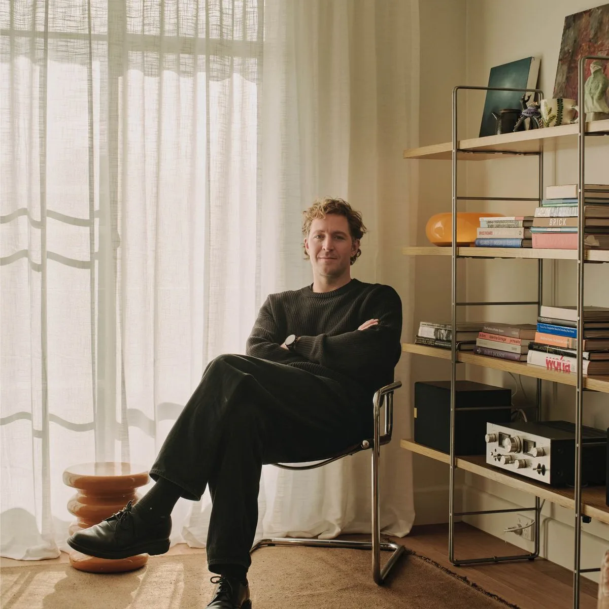 A player sitting in a chrome chair in a bright living room with bookshelves