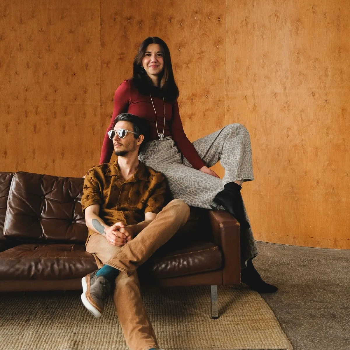 Two players posing on a leather sofa against a wood-panelled wall
