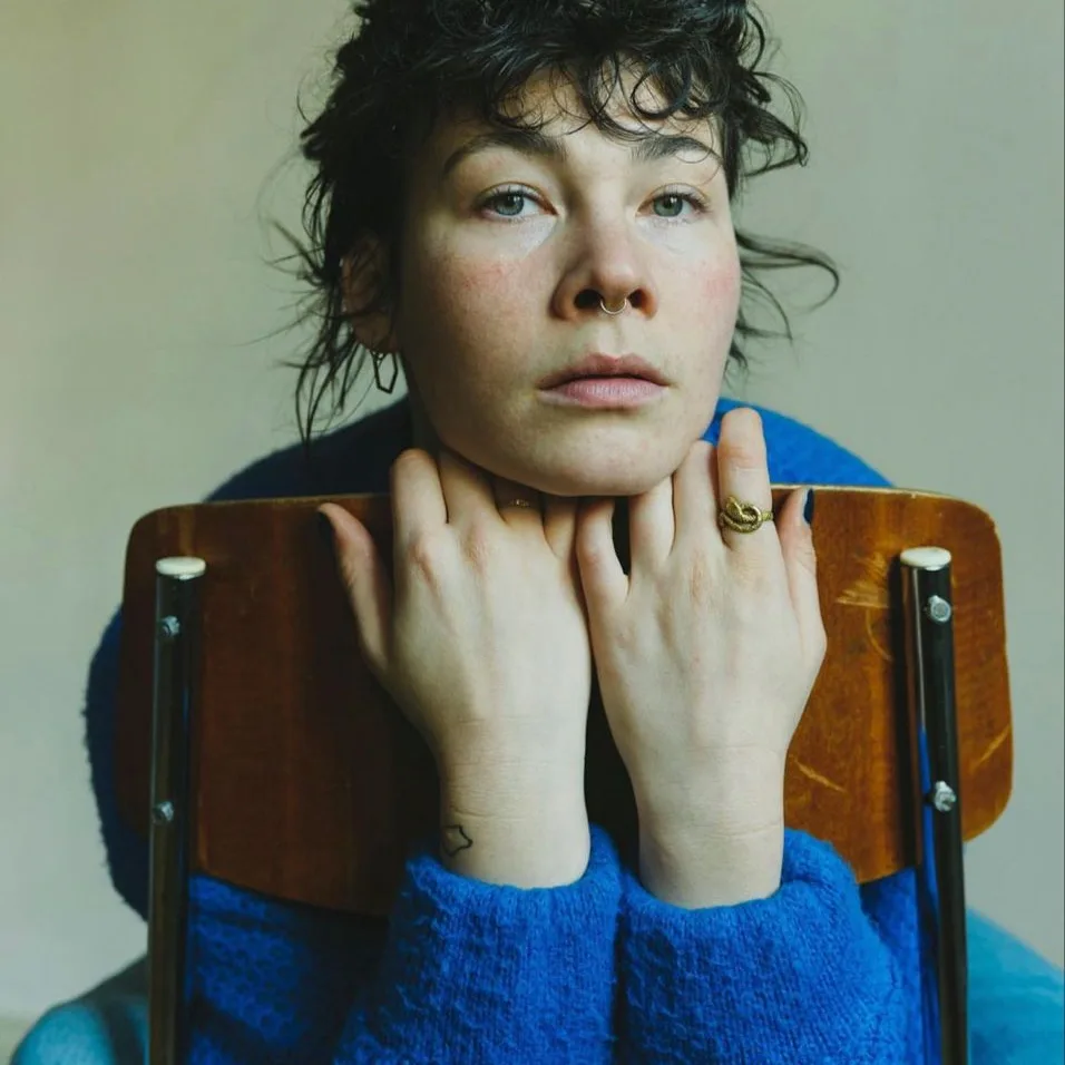 Portrait of a player in a blue sweater resting her hands on the back of a wooden chair
